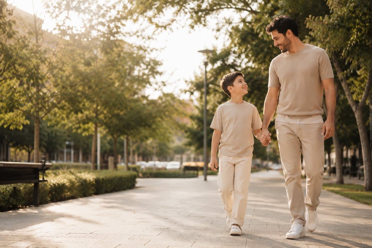 Un niño camina relajado de la mano de su papá por una plaza soleada